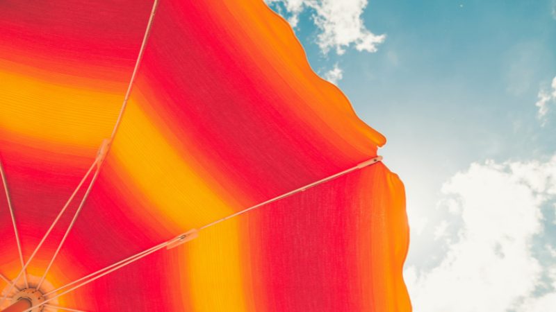 Orange and red umbrella underneath a blue sky with clouds. 
